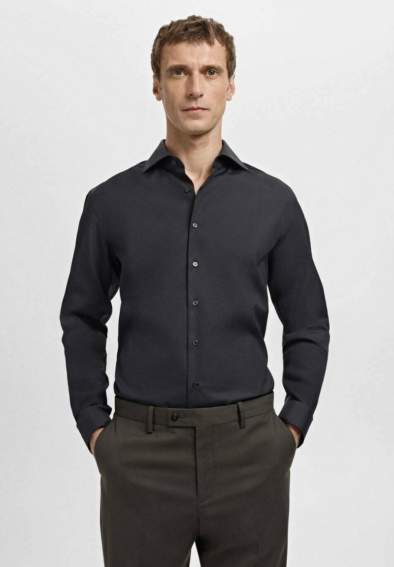 Zwarte blouse met lange mouwen en knopen, klassieke kraag, gladde textuur en subtiele glans, gecombineerd met donkere broek.