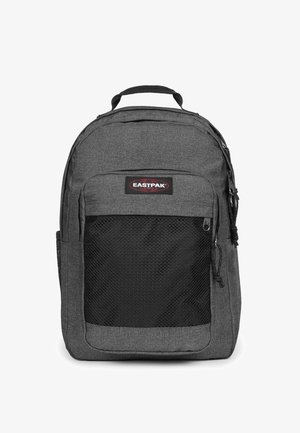 Mochila de tela gris con un bolsillo delantero de malla negra, doble cremallera y un asa en la parte superior para llevar. Logotipo visible en la parte frontal.