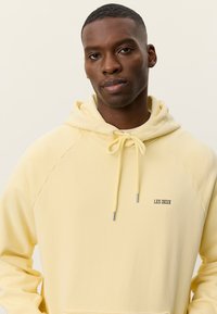 Κίτρινο φούτερ με κορδόνι, με μπροστινή τσέπη καγκουρό και μαύρο λογότυπο "LES DEUX" στο αριστερό στήθος. Απαλό ύφασμα από βαμβακερό μείγμα.