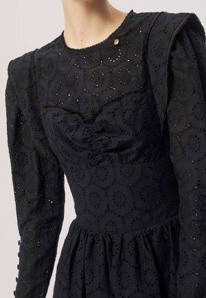 Vestito nero a maniche lunghe con motivi floreali a occhiello, spalle imbottite, corpetto aderente e piccolo bottone dorato vicino allo scollo.