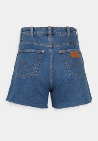 Farkkutrikoot keskipainoisessa sinisessä, raidoitettu alaosa, kaksi takataskua ja ruskeasta nahasta valmistettu merkki vyötäröllä. Ompeleet taskuissa.