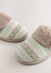 Pantofole lavorate a maglia in morbido beige, verde e crema con polsino in pelliccia sintetica. Punta arrotondata, superficie testurizzata e suola piatta in gomma.