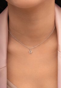 Silberne Halskette mit einem Sternanhänger, ausgestattet mit einer feinen Kette und einem zarten offenen SternDesign. Getragen auf einem glatten, hellen Stoff.