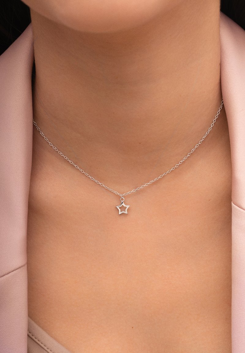 Silberne Halskette mit einem Sternanhänger, ausgestattet mit einer feinen Kette und einem zarten offenen SternDesign. Getragen auf einem glatten, hellen Stoff.