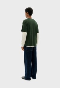 Groene korte mouwen T-shirt over een crèmekleurig lange mouwen shirt, gecombineerd met loszittende blauwe denim pants. Eenvoudig ontwerp, casual pasvorm.