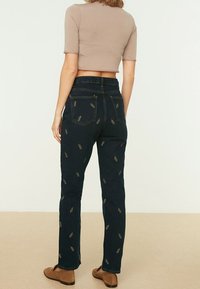 Jeans de denim azul oscuro con bordado de hojas doradas, cintura alta y corte recto. Acompañados de un top corto ajustado beige.
