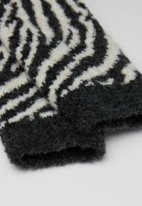 Gants pelucheux rayés noir et blanc avec une texture douce, présentant des motifs de vagues irréguliers et un design de poignet replié.