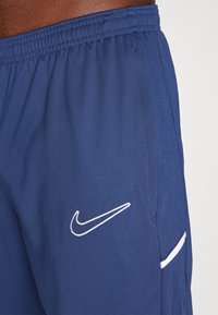 Jūras spēku sporta šorti, kas izgatavoti no elpojoša auduma ar elastīgu jostu, ar baltu Nike logo un kontrastējošām akcenta svītrām.