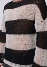 Maglione a righe con strisce orizzontali nere e crema, realizzato in un tessuto leggero e a maglia aperta. Ha una vestibilità rilassata e un colletto a girocollo.