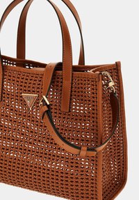 Sac fourre-tout tissé marron avec des anses en cuir, arborant un logo en métal triangulaire et des accents noirs. Surface texturée avec une forme structurée.
