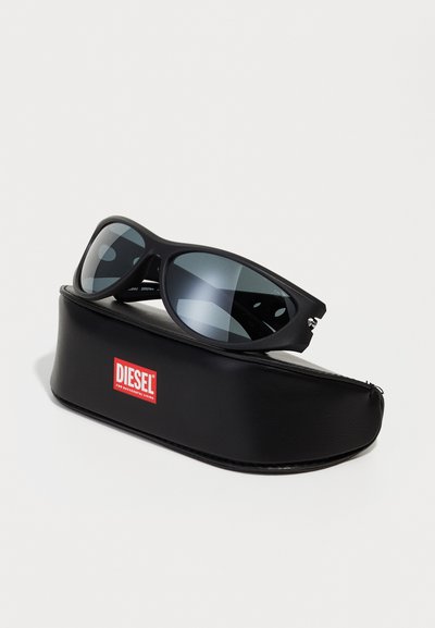 Lunettes de soleil noires avec une finition mate, verres teintés gris et un étui en cuir noir arborant un logo rouge Diesel. Design sportif distinctif.