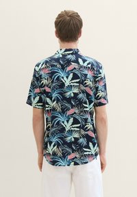 Camisa de manga corta con un fondo azul marino oscuro y un vibrante patrón de hojas tropicales en tonos rosa, verde y azul, hecha de una tela ligera.