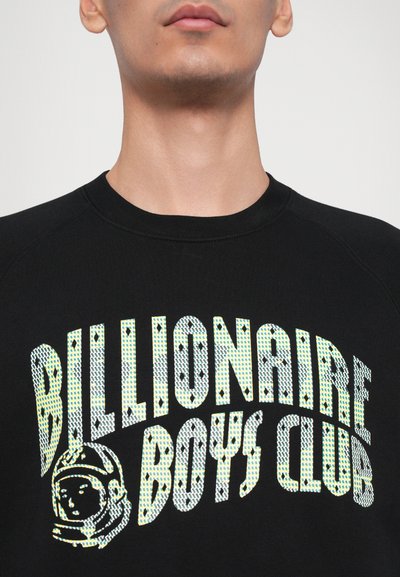 Melna pūkainā krekls ar uzrakstu "Billionaire Boys Club" tekstūrētā, atstarojošā burtu stilā un astronauta grafiku. Ierobežota apkakle un pleci.