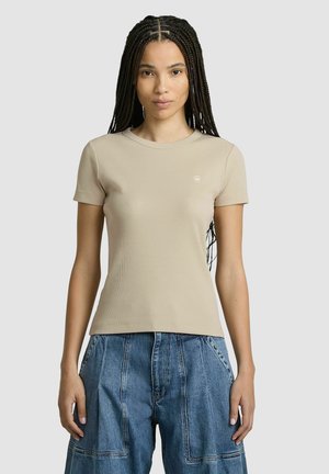 T-shirt à manches courtes en rib, beige, avec un col rond et un détail logo discret sur la poitrine, associé à un pantalon en denim à jambes larges.