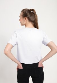 Biała koszulka z krótkim rękawem, widoczna od tyłu, z okrągłym dekoltem i luźnym krojem, zestawiona z czarnymi dżinsami.