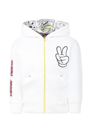 Haut de survêtement zippé blanc avec fermeture éclair jaune et signe de paix brodé à l'avant. La doublure de la capuche présente un impression de bandes dessinées en noir et blanc. Texte rouge sur les manches.