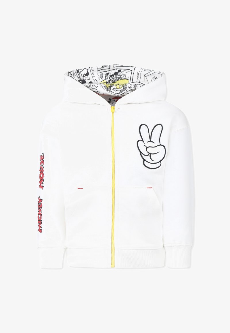 Haut de survêtement zippé blanc avec fermeture éclair jaune et signe de paix brodé à l'avant. La doublure de la capuche présente un impression de bandes dessinées en noir et blanc. Texte rouge sur les manches.