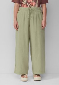 Lichtgroene broek met wijde pijpen, elastische tailleband en trekkoord. Geчастый stof, dat zacht aanvoelt, gestyled met een gebloemde top met patroon.
