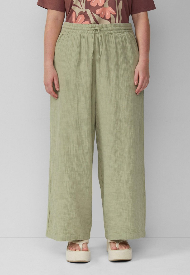 Lichtgroene broek met wijde pijpen, elastische tailleband en trekkoord. Geчастый stof, dat zacht aanvoelt, gestyled met een gebloemde top met patroon.