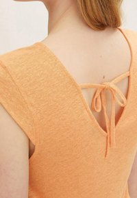 Close-up of a woman's upper back wearing a peach knit top with a V-back and a tied bow detail.