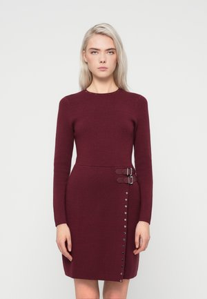 Burgundy mekko, jossa on pitkät hihat, pyöreä pääntie, sivun soljet ja nappidetails vasemmalla puolella. Valmistettu teksturoidusta neulemateriaaleista.