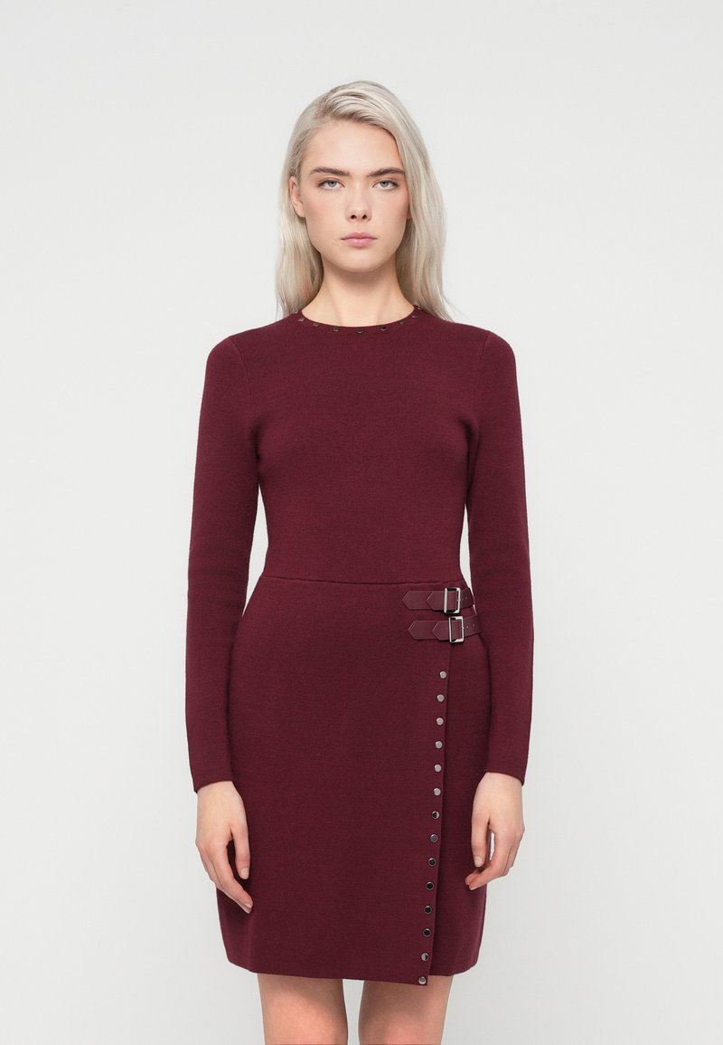 Bordo haljina s dugim rukavima, okruglim izrezom, bočnim kopčama i detaljima s gumbima duž lijeve strane. Izrađena od teksturirane pletive.