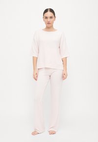 Gaiši rozā mājīgais apģērbu komplekts, kas sastāv no īsām piedurknēm topa ar apaļu kakla izgriezumu un taisnās kāju biksēm; izgatavots no mīksta, teksturēta auduma.