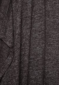 Tmavě šedá pletenina s texturovaným, mírně melírovaným vzhledem. Materiál je měkký, má volný splývavý tvar a minimálně viditelné švy.