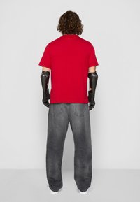 Punane lühikeste varrukatega T-särk, lõdvad hallid teksased, mustad kindad proteeskäte peal. Lihtne disain ja mugav lõige, sobib igapäevaseks kandmiseks.