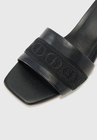 Svarte lær sandle med bred, strukturert stropp som har et logomønster. Kvadratisk tådesign og glatt, polert finish.
