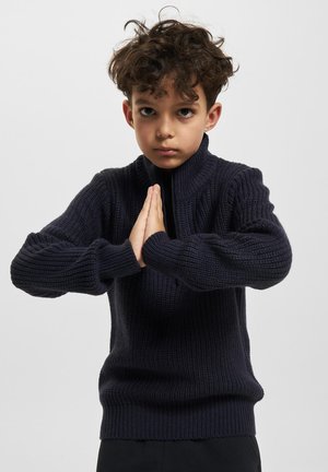 Pull en maille bleu marine avec un col montant et une texture côtelée. Il possède des manches longues et une taille cintrée, mettant en avant un design décontracté.