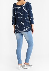 Blusa blu navy con motivo astratto bianco, maniche a tre quarti, abbinata a jeans skinny azzurri e scarpe slip-on argentate.