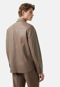 Brun læderjakke med straight snit, spidst krave og manchet med knapper. Har en glat tekstur og minimale syningsdetaljer.