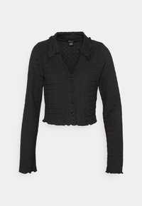 Cárdigan corto negro de tejido texturizado, con mangas largas y un cuello con volantes. Cinco botones en la parte delantera añaden detalle.