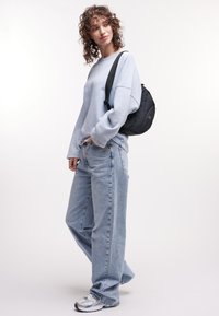 Ljusblå oversized sweatshirt, ljus tvättade baggy jeans, svart ryggs�äck och silverfärgade sportskor med grå detaljer. Lockigt hår.