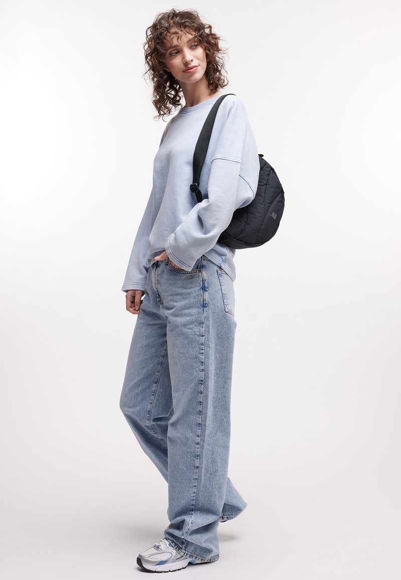 Felpa oversize blu chiaro, jeans baggy in denim chiaro, zaino nero e scarpe da ginnastica argentate con accenti grigi. Capelli ricci.
