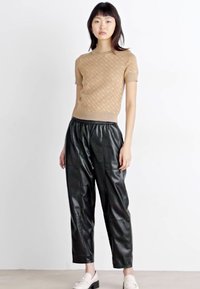 Μπεζ πουλοβεράκι κοντό μανίκι με υφή, συνδυασμένο με γυαλιστερά μαύρα παντελόνια από ψεύτικο δέρμα. Τα παπούτσια είναι λευκά με επίπεδο τακούνι.