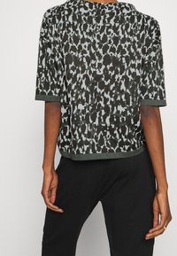 Haut en maille à motifs verts et bleu clair, coupe décontractée, manches courtes et encolure ronde. L'ourlet arrive à la taille.