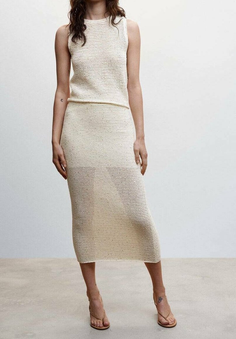 Completo in maglia a due pezzi color avorio, composto da un top senza maniche e una gonna midi aderente con un motivo testurizzato. Sandali completano il look.