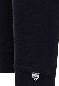 Sort strikket stof med et lille hvidt mærke med en blå bi-logo syet tæt på kanten af tøjet.