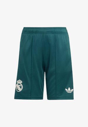 Dos jóvenes jugadores de fútbol de pie, con camisetas verdes del Real Madrid, pantalones cortos a juego, calcetas altas y botas negras con detalles rojos.