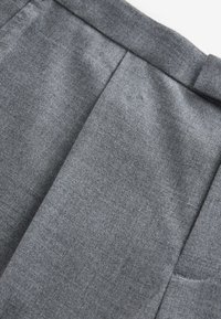 Pantalon en tissu gris avec une texture lisse, des plis cousus et une coupe droite ; comprend une ceinture et des poches latérales.