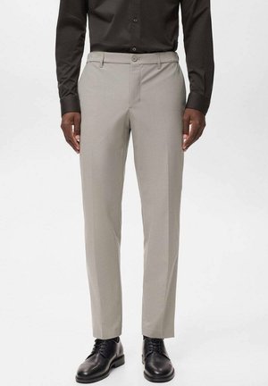 Pantaloni grigi chiari con una vestibilità su misura, dotati di chiusura a bottone e zip, tasche laterali e una texture liscia, abbinati a scarpe nere.