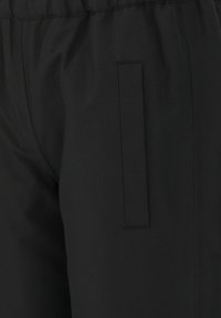Un pantalon en tissu noir au toucher lisse, doté d'une taille élastique et d'une poche fendue sur le côté droit, conçu pour le confort.