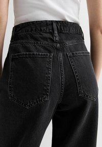 High-waisted black denim jeans with a smooth texture, featuring two back pockets and stitched detailing along the seams.