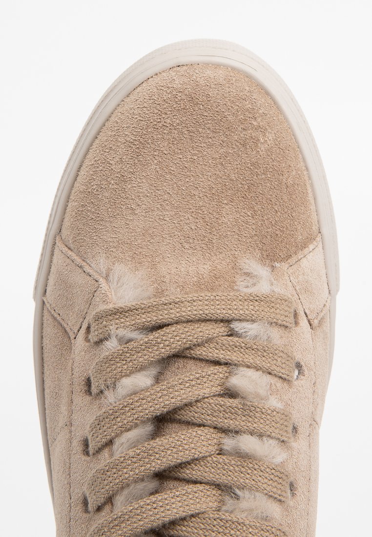 Beige Wildleder-Sneaker mit strukturiertem Material, runder Zehenform, flachen Schnürsenkeln und Gummisohle. Auffällige flauschige Akzente in der Nähe der Ösen.