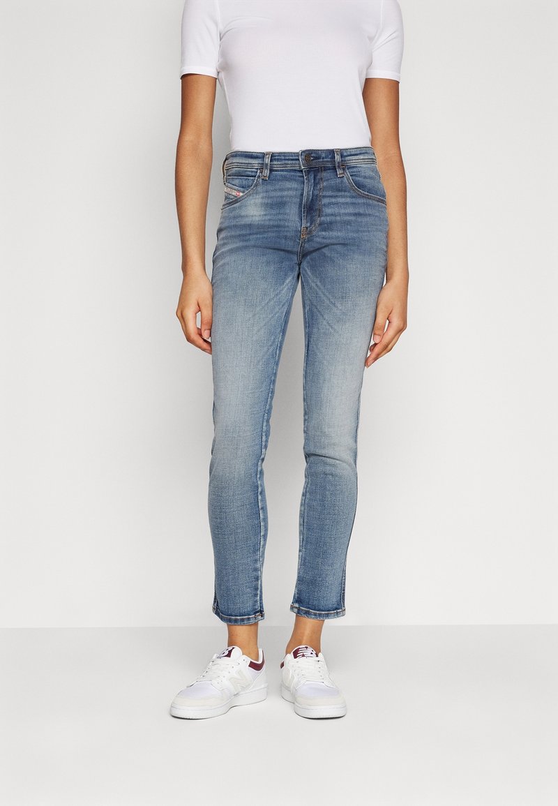 Jasnoniebieskie wąskie dżinsy o wyblakłym wykończeniu, z pięcioma kieszeniami i średnim stanem, zestawione z białymi adidaskami i dopasowaną białą koszulką.