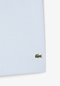 T-shirt en coton bleu clair à manches courtes, avec un petit logo de crocodile vert brodé dans le coin inférieur gauche.