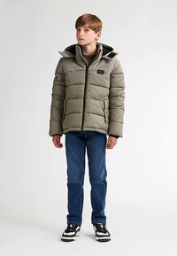 Grå polstret jakke med hætte, lynlåslukning og logo-patch. Stylet med blå jeans og sorte sko, med en glat tekstur og vandrette linjer.