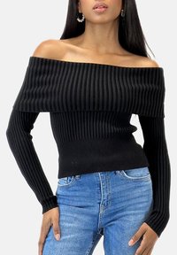 Maglione nero a coste con scollo a barca e maniche lunghe, caratterizzato da una silhouette aderente e tessuto strutturato, abbinato a jeans azzurri.